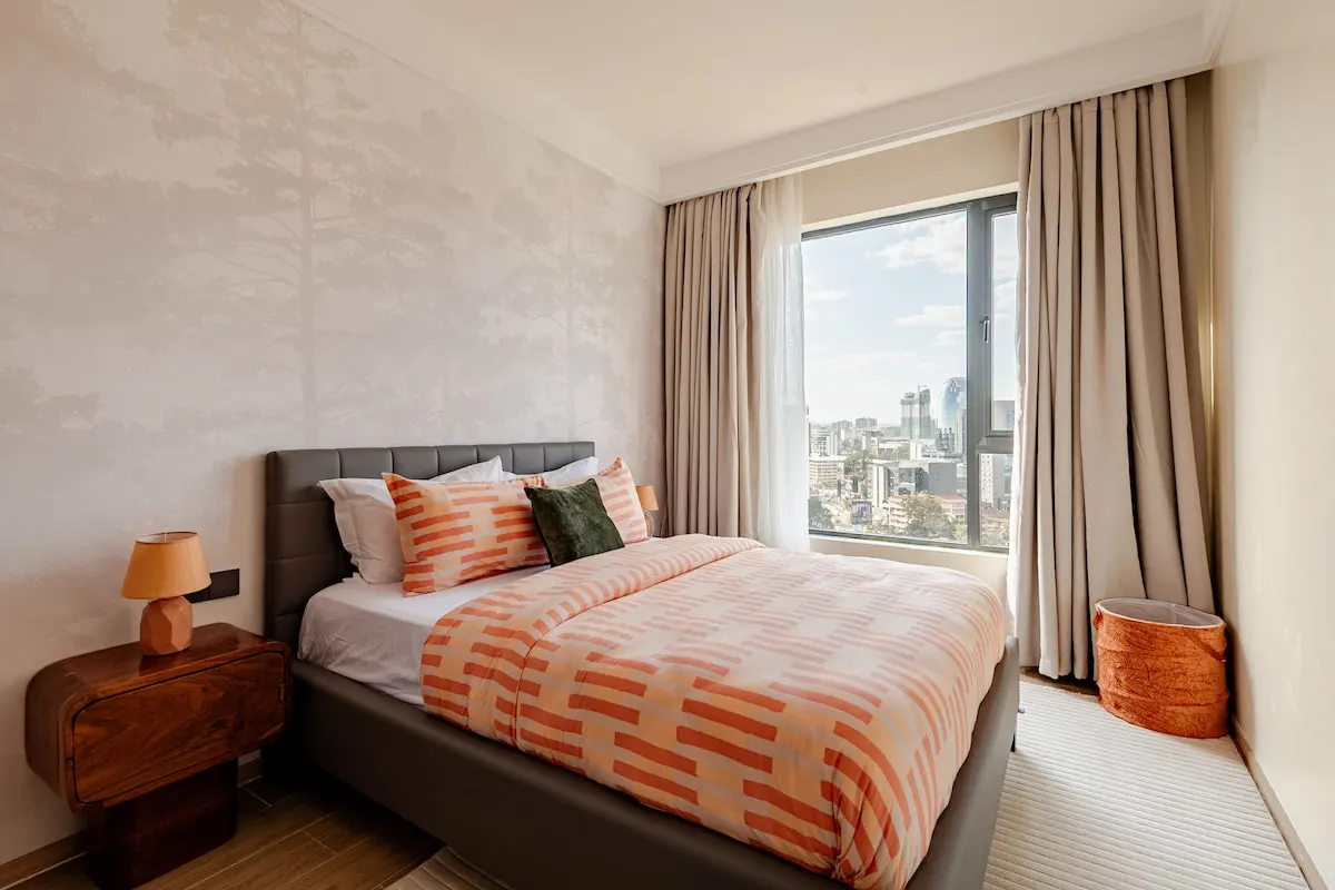 Bedroom with a queen bed, orange patterned bedding and a city view